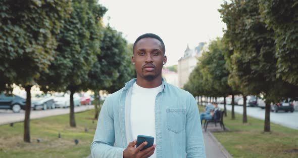 Man which Standing in the Middle of Urban Alley with Green trees and Looking at Camera