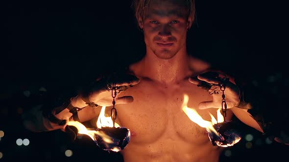 Young Blond Male Holds Two Burning Pois Hanging on Chains. Slow Motion. Close-up