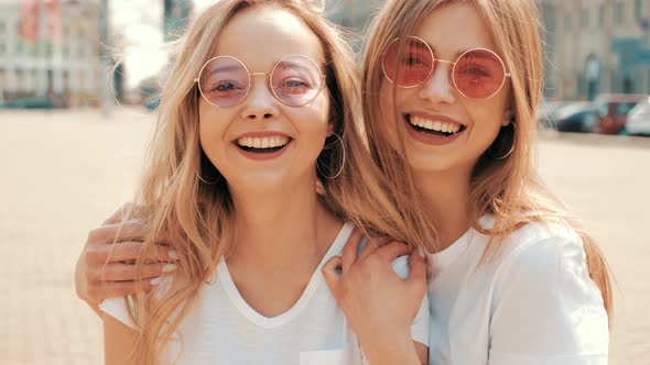 Two young beautiful blond smiling hipster girls in trendy summer clothes