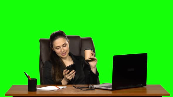 Business Woman Sitting at Desk in Leather Chair Writes Message on Cell Phone and Drink Coffee. Green