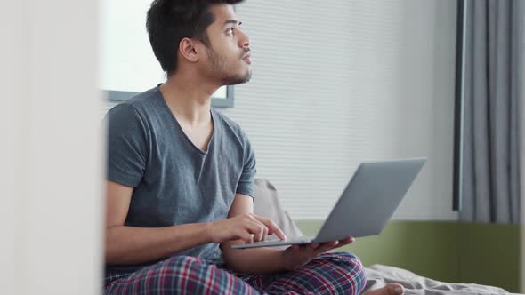 Pensive Indian man wearing pajama having an idea while working on laptop