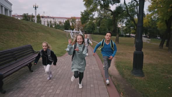 Front View of Caucasian Schoolkids with Schoolbags Running in the School Yard at School
