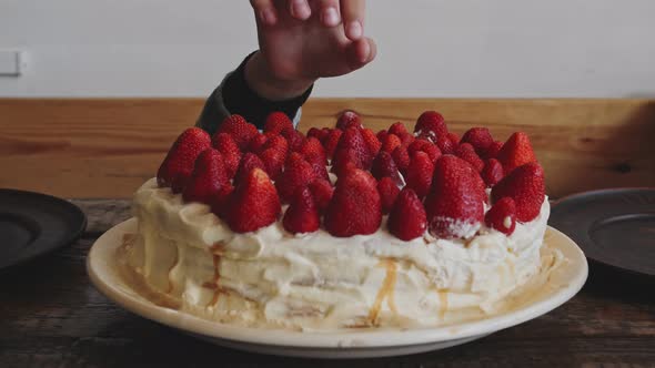 Baby Hand Takes Strawberries From Cake Decorated with Whipped Cream and Strawberries