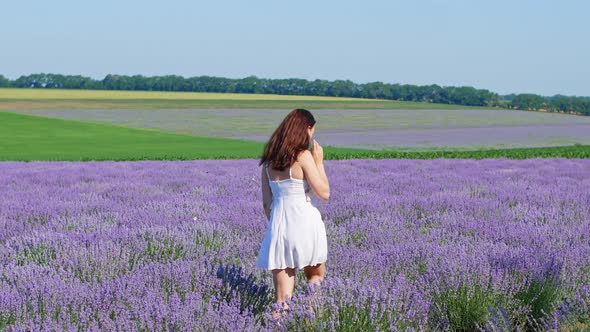 A woman in a white dress walks through a lavender field. A beautiful girl in a white dress