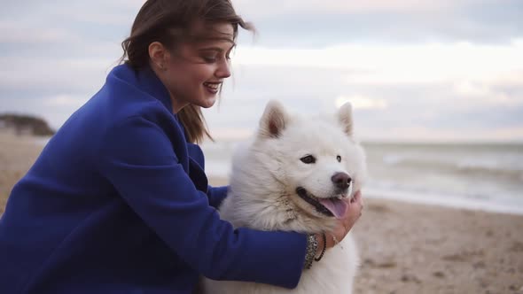 Young Woman Sitting on the Sand and Stroking Her Dog of the Samoyed Breed By the Sea