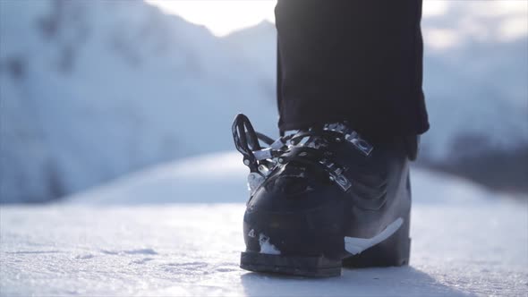 A woman with ski boots preparing to go skiing in the snow at a ski resort.