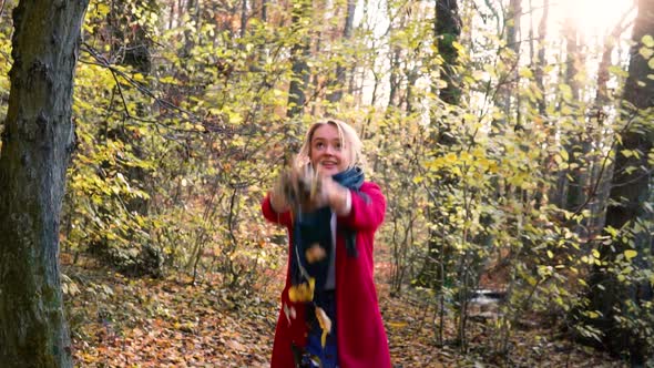 SLOWMOTION Young beautiful woman throwing leaves in the air amidst thee orange brown autumn forest w