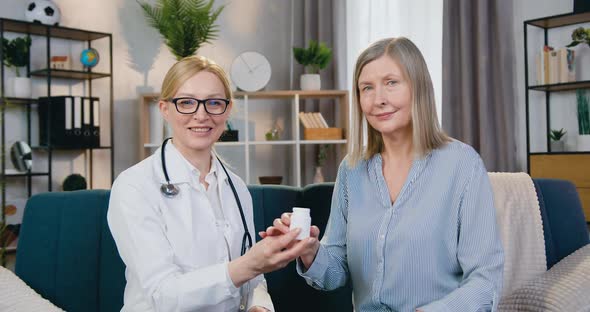 Doctor and Patient Sitting in front of Camera with Sincerely Smiles and Holding Bottle with Vitamins
