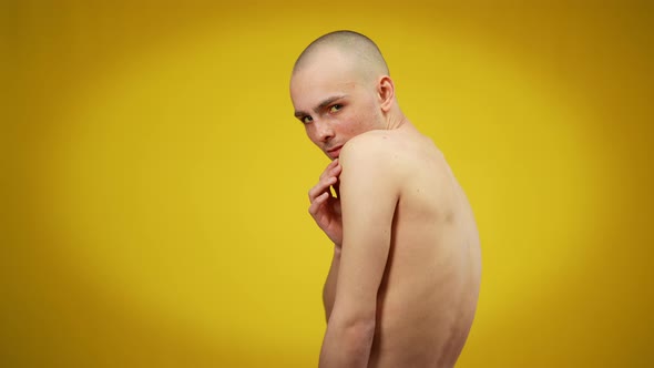 Side View Medium Shot of Young Caucasian Male Queer Looking at Camera Posing at Yellow Background