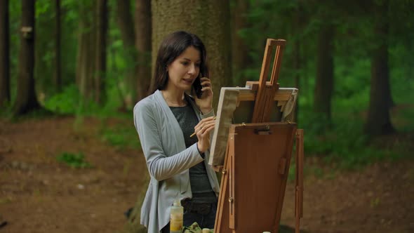 Girl Artist Painting a Picture in the Park and Talking By the Phone