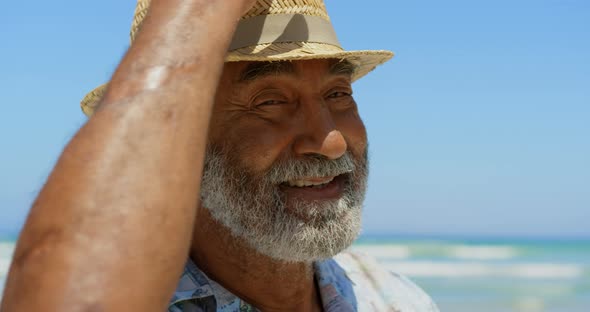 Front view of active senior African American man with hat standing on beach in the sunshine 4k