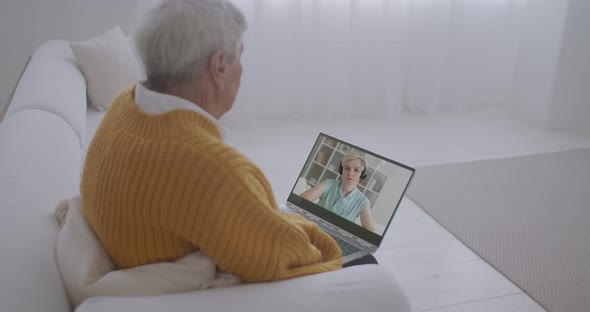 Elderly Man Is Communicating with His Adult Daughter By Video Call at Screen of Notebook, Sitting on