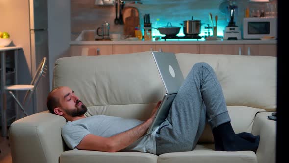 Man Falling Asleep in Fron of TV While Working on the Laptop