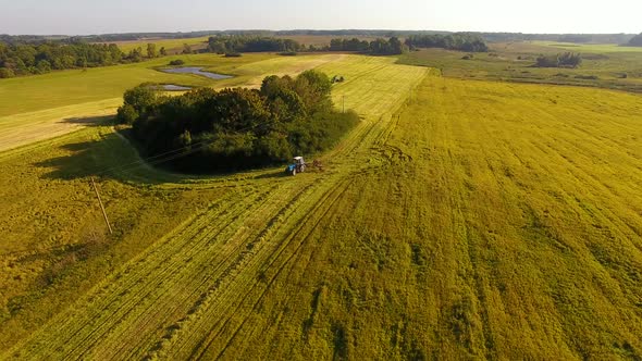 The tractor is stacking haystacks on an agricultural field in autumn, aerial view