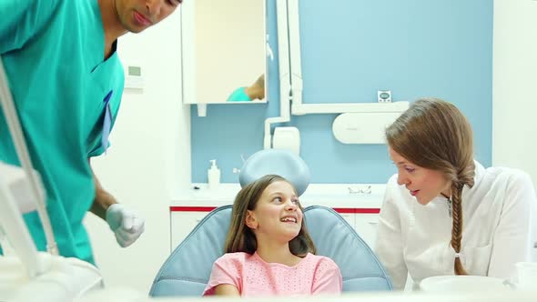 Friendly dentist talks with young patient while assistant examines her