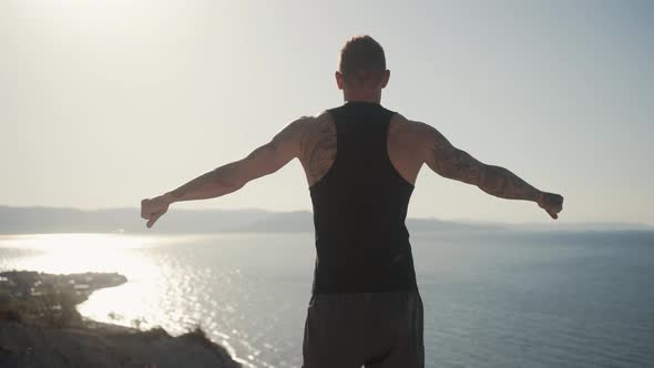 Backside View of Tattooed Muscular Man Does Workout Outdoors on Top of Mountain