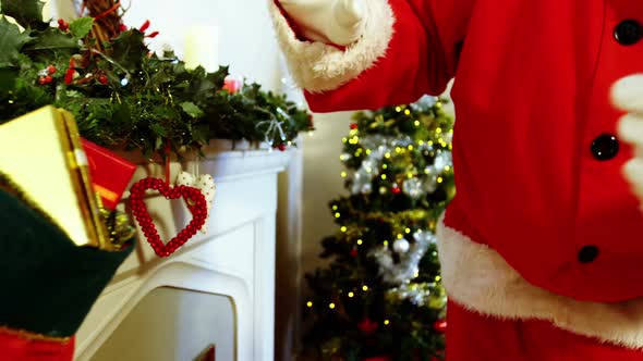 Mid section of santa claus placing gift box on fireplace