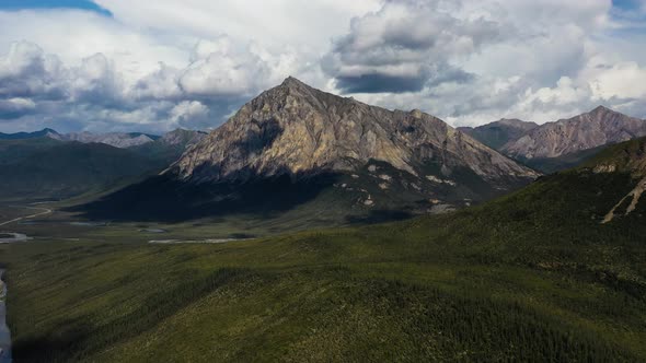 Aerial flying over green forest valley towards Sukakpak Mountain against rain clouds in Summer Alask