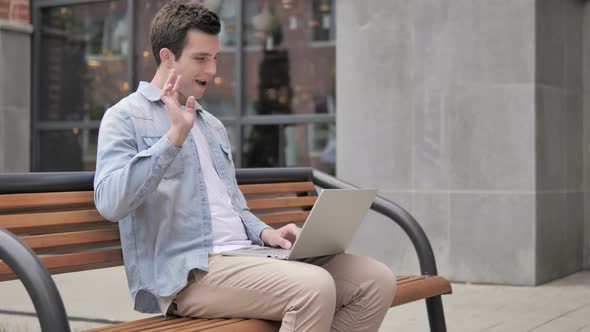 Online Video Chat on Laptop by Young Man Sitting on Bench