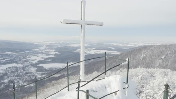 A Cross at a Lookout with a View on a Snowcovered Mountainous Winter Landscape