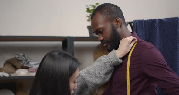 Corean Female Tailor Measuring Black Man in Workshop