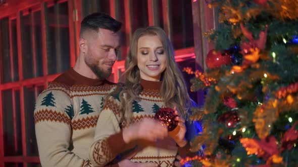 Handsome man and beautiful woman decorate New year tree with christmas balls. 