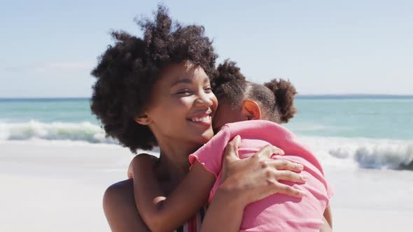 Smiling african american mother with daughter embracing on sunny beach