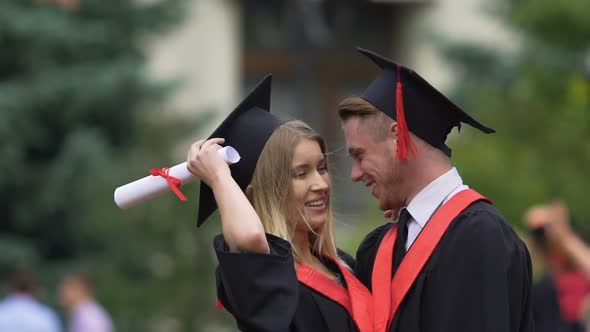 Pretty Lady in Academic Dress Hugging Boyfriend and Smiling Graduation Party