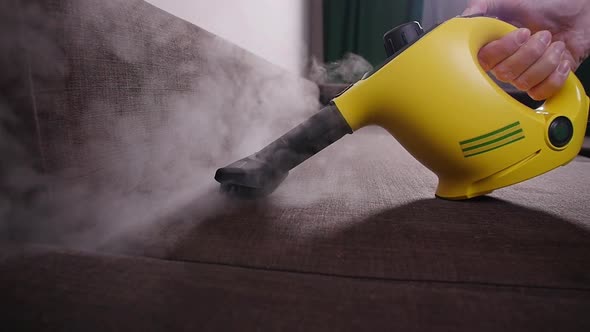 Furniture Cleaning Concept. Cleaning the Sofa with an Antibacterial Steam Cleaner