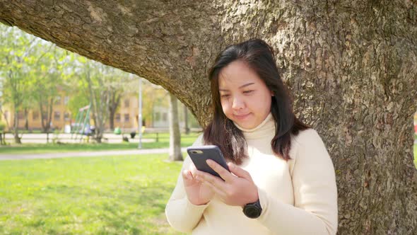 Asian woman with black straight hair and happy face. Standing and using her smart phone