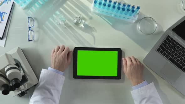 Researcher Looking at Tablet With Green Screen, Results of His Chemical Research