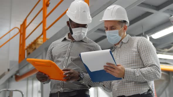 Industrial Supervisors in Safety Helmet and Medical Mask Doing Report on Digital Tablet 