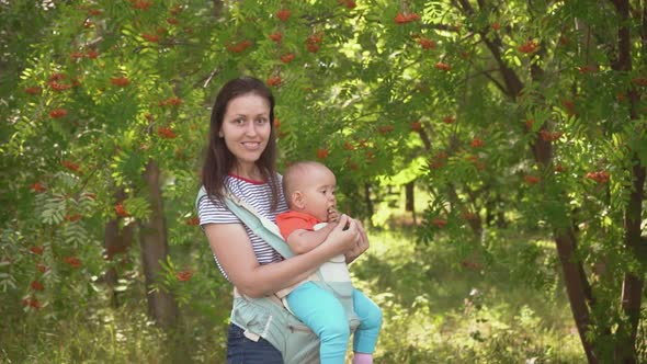 Mom walks with a newborn baby in the park, a child in a sling - a special carrier bag for children.