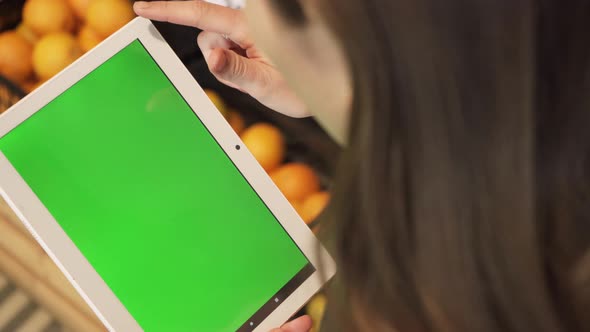 Closeup of a Young Woman's Hand Holding a Tablet Computer with a Green Screen Layout