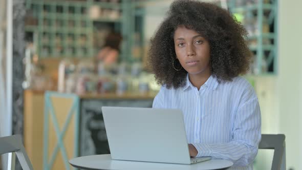 African Woman with Laptop Looking at Camera in Cafe 