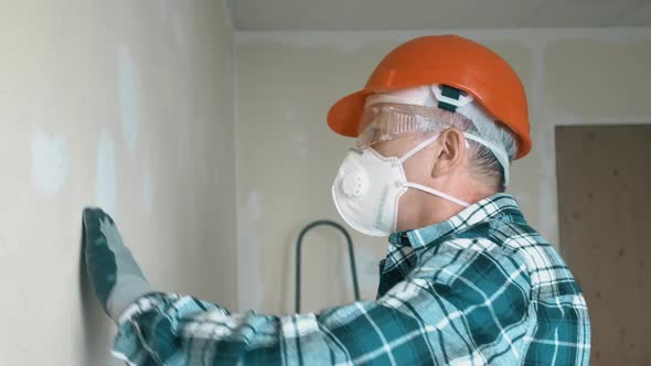 An Elderly Man Master Levels a Wall with a Tool in an Orange Helmet and Protective Glasses While