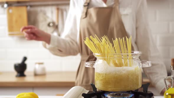 Cooking Spaghetti In A Transparent Saucepan. Woman Cooks Pasta. Hostess Listens To Music, Dances