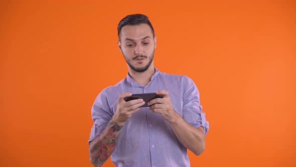 Handsome Man Playing With His Smartphone And Winning On An Orange Screen