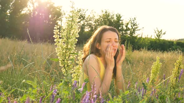 Pretty Young Girl is Sitting in the Middle of the Field with Flowers During Summer Time and Sneezing