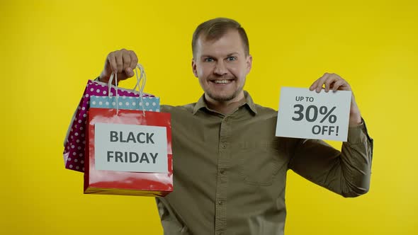 Man Showing Shopping Bags and Up To 30 Percent Off Inscription, Looking Satisfied with Low Prices