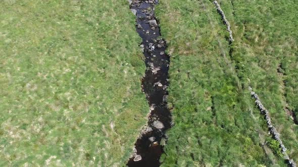 Wide-shot aerial birdseye view tracking forward and downwards over a river and a man-made stone wall