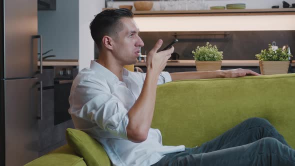 Young Man Resting on Sofa Holding Smartphone Calling Using Speaker Phone. Cheerful Male Using Mobile