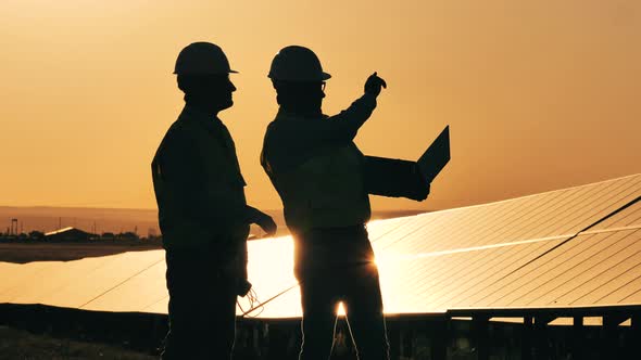 Two Solar Power Engineers Working on a Solar Farm at Sunset