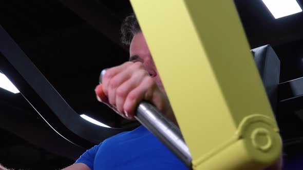 A Young Fit Man Trains on a Machine in a Gym - Face Closeup From Below
