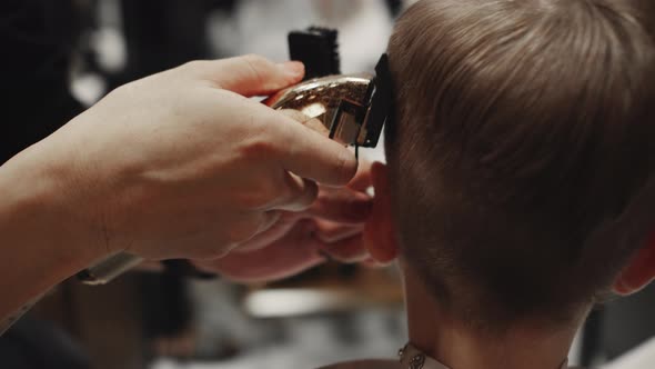 Fashionable Hairdresser Cuts a Child's Hair with a Clipper in a Barbershop