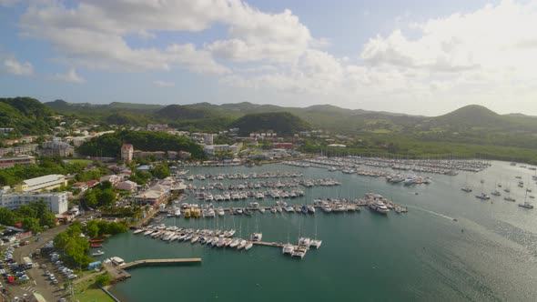 Aerial of green mountains, settlement and boats moored at marina harbor