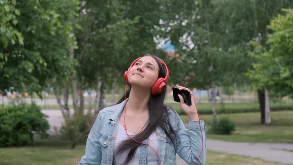 Cheerful Girl in Headphones Walks on the Street