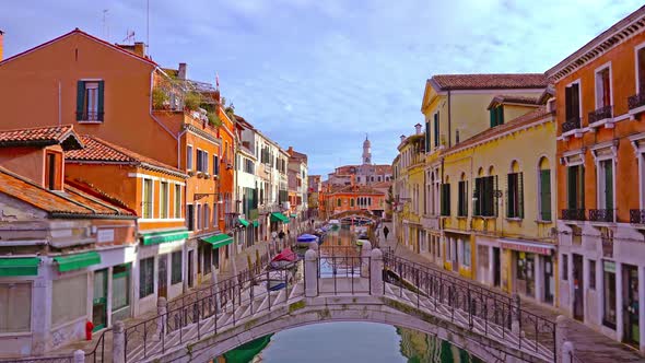 Bridge Over Narrow Canal with Boats Among Colorful Buildings