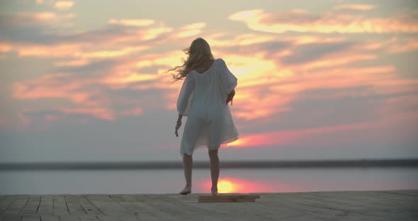 Happy Woman in White Dress is Dancing on the Pier of the Lake Sunset Sky