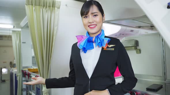 Portrait of Asian flight attendant smiling greeting welcome to passenger on board in airplane cabin.